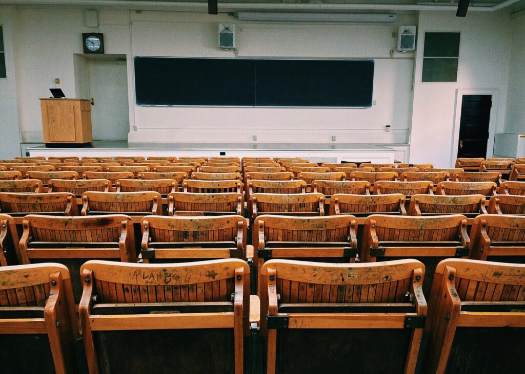 photo of a college classroom with a chalkboard and podium at the front and rows of wooden chairs